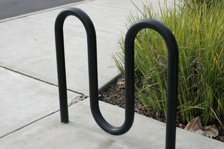 A black road bicycle locked to a green inverted
